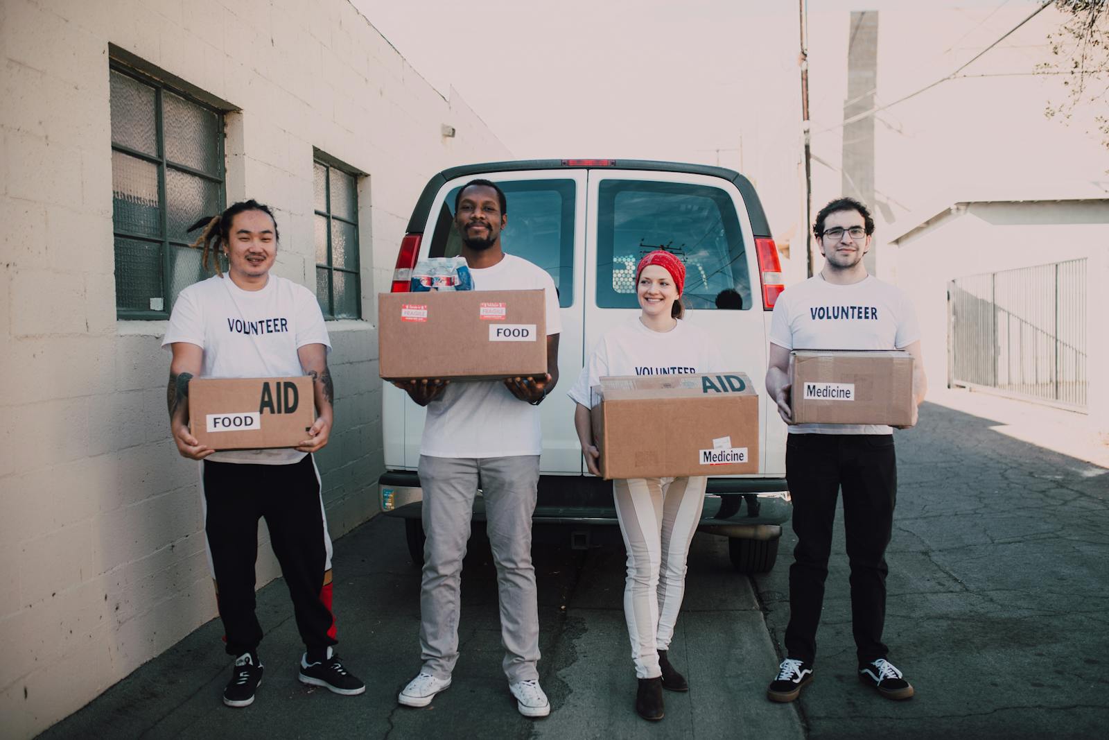 Volunteers holding aid boxes beside a delivery van.